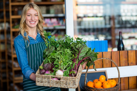 Portrait of a smiling staff holding a basket of fresh vegetables in organic section of supermarketの写真素材