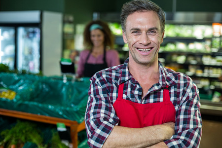 Portrait of smiling male staff standing with arms crossed in organic section of super marketの写真素材