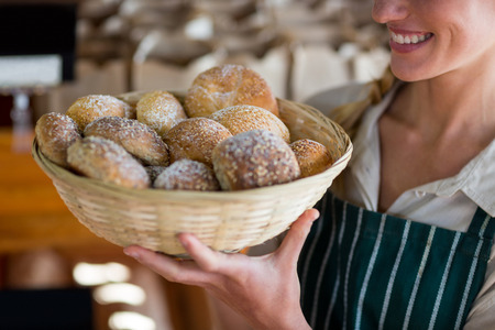 Mid section of smiling female staff holding basket of sesame breads at bread counter in supermarket