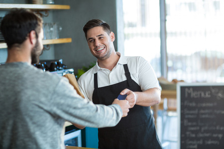 Smiling waiter giving bread to customer at counter in cafeの写真素材