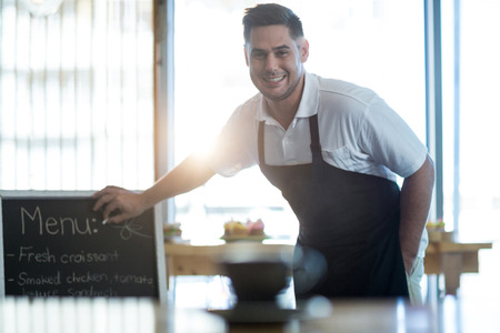 Portrait of smiling waiter writing on menu board in cafeの写真素材