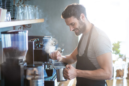 Smiling waiter making cup of coffee in cafeの写真素材