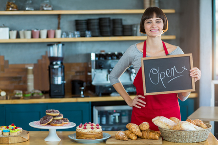 Portrait of smiling waitress showing slate with open sign in cafeの写真素材