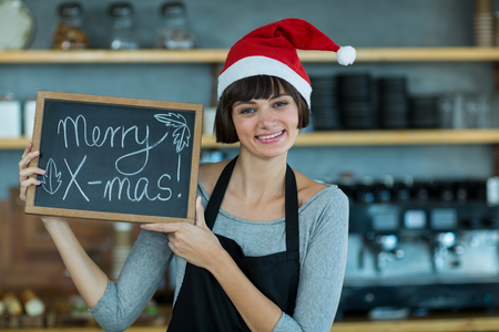 Portrait of waitress showing slate with merry x-mas sign in cafÃ©の写真素材
