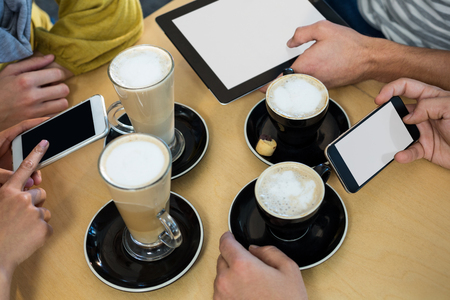 Friends using mobile phone and digital tablet while having cup of coffee in cafÃ©の写真素材