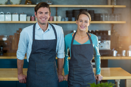 Portrait of smiling waiter and waitress standing at counter in cafeの写真素材