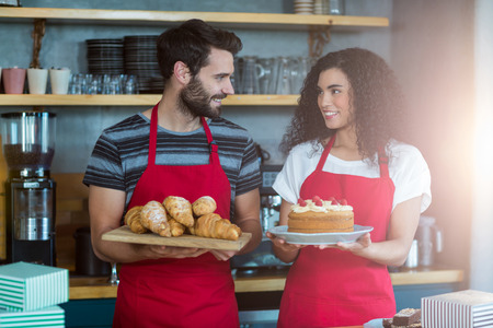 Smiling waiter and waitress holding a tray of croissants and cake in cafÃ©