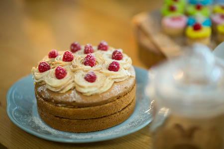 Sponge cake with whipped cream and cherry topping on plate in cafÃ©の写真素材