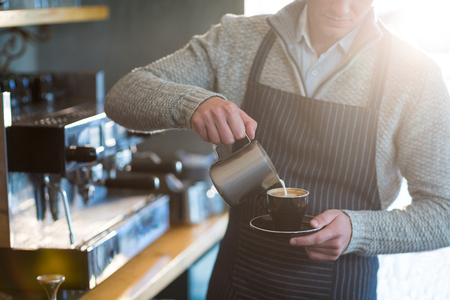 Mid-section of waiter making cup of coffee at counter in cafeの写真素材
