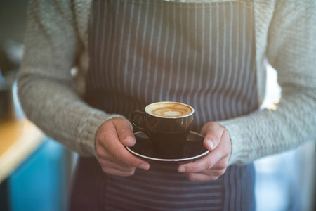 Mid-section of waiter holding cup of coffee in cafÃ©の写真素材