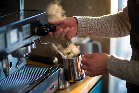 Waiter making cup of coffee at counter in kitchen at cafÃ©の写真素材