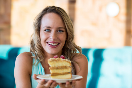 Excited woman holding pastry on plate in cafe