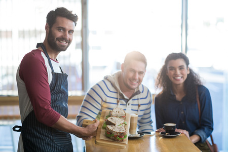 Portrait of waiter serving a plate of sandwich to customer in cafeの写真素材
