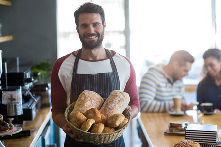 Portrait of smiling waiter holding a basket of bread in cafÃ©の写真素材