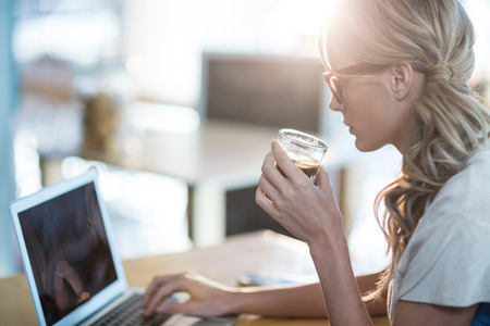 Woman using a laptop while having cup of coffee in cafeの写真素材