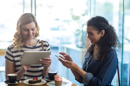 Women using mobile phone and digital tablet while having cup of coffee in cafÃ©の写真素材