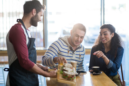 Waiter serving a plate of sandwich to customer in cafe
