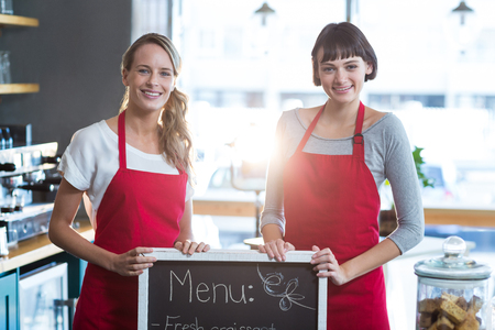 Portrait of smiling waitress standing with menu board in cafeの写真素材