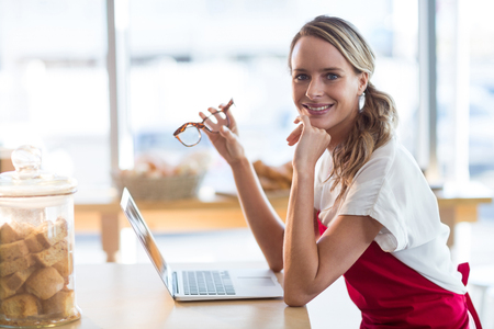 Portrait of smiling waitress sitting at table and using laptop in cafÃ©の写真素材