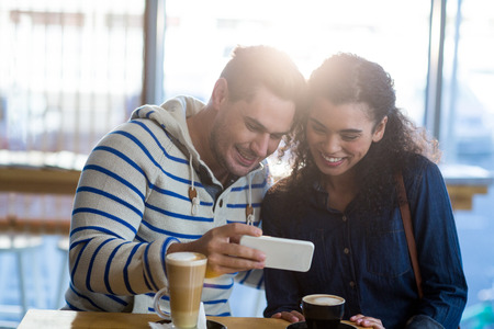 Couple using mobile phone while having a cup of coffee in cafÃ©の写真素材
