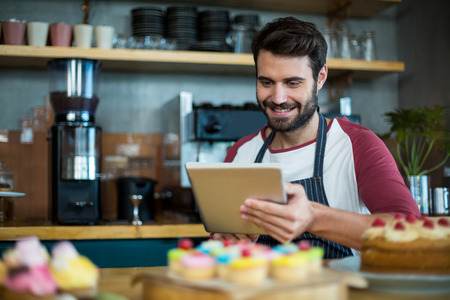 Smiling waiter using digital tablet at counter in cafeの写真素材