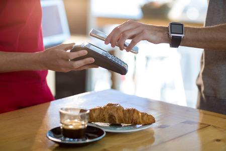 Man paying bill through smartphone using NFC technology in cafe