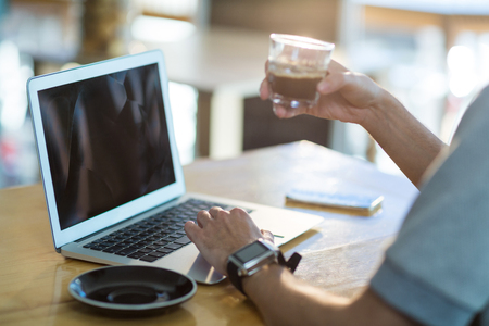 Man using a laptop while having cup of coffee in cafeの写真素材