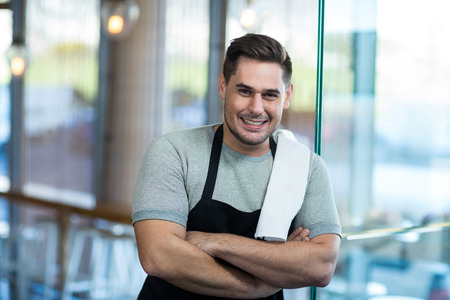 Portrait of smiling waiter leaning on glass door in cafÃ©の写真素材