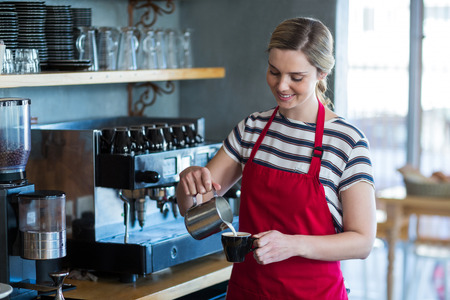 Smiling waitress making cup of coffee at counter in cafeの写真素材
