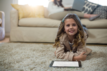 Girl using digital tablet while lying on the floor at homeの写真素材