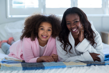 Portrait of mother and daughter lying on bed at homeの写真素材