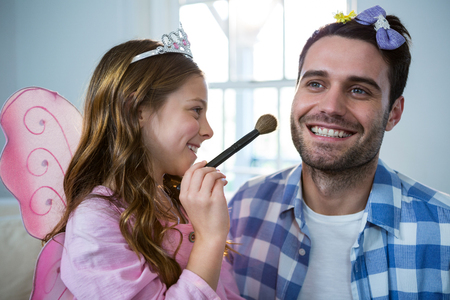 Girl dressed up in a fairy costume applying make-up on fathers face at homeの写真素材