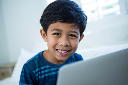 Portrait of boy using laptop while relaxing on bed in the bedroomの写真素材