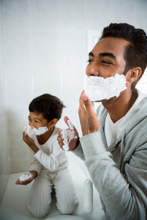 Father and son applying foam on face together in the bathroom at homeの写真素材