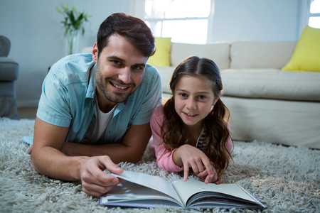 Portrait of father and daughter reading book in the living room at homeの写真素材