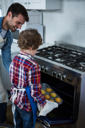 Father and son placing cupcakes tray in oven in the kitchenの写真素材