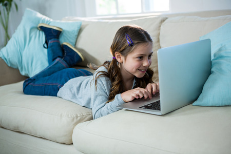 Girl relaxing on sofa and using laptop in the living room at homeの写真素材