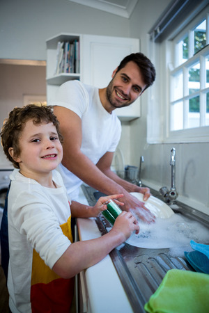 Portrait of son helping father in washing utensils in the kitchen sinkの写真素材