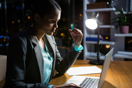 Businesswoman working on laptop in office at nightの写真素材