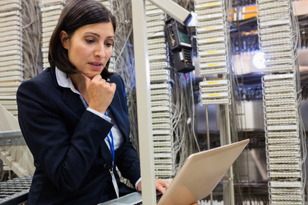 Thoughtful technician working on laptop in server room