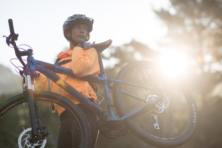 Female biker carrying mountain bike and walking in countrysideの写真素材