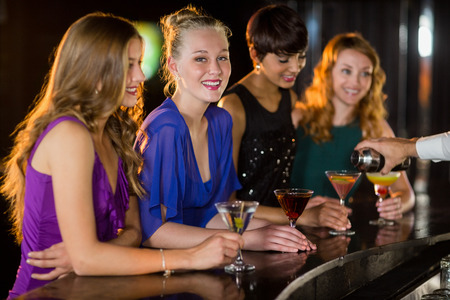 Smiling woman with cocktail standing at bar counter with her friendsの写真素材