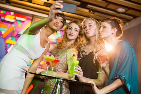 Group of friends taking selfie from mobile phone while having cocktail in barの写真素材