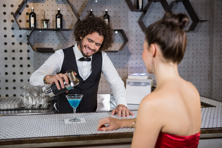 Waiter pouring cocktail in womans glass at bar counter in barの写真素材