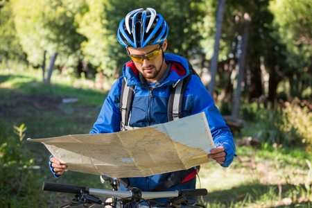 Male mountain biker looking at map in the forestの写真素材
