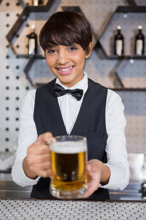 Barmaid serving glass of beer at bar counter in barの写真素材
