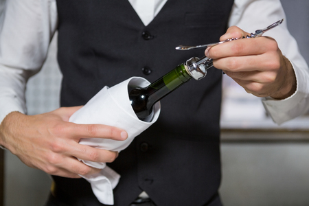 Bartender using corkscrew to open wine bottle in barの写真素材