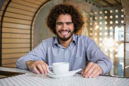Portrait of man sitting on bar counter with cup of tea in barの写真素材