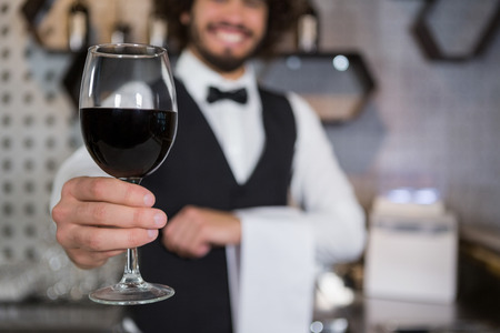 Portrait of smiling bartender serving glass of red wine in bar counter at barの写真素材
