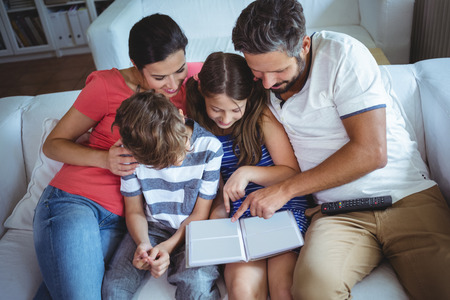 Family sitting on sofa and looking at a photo album at homeの写真素材